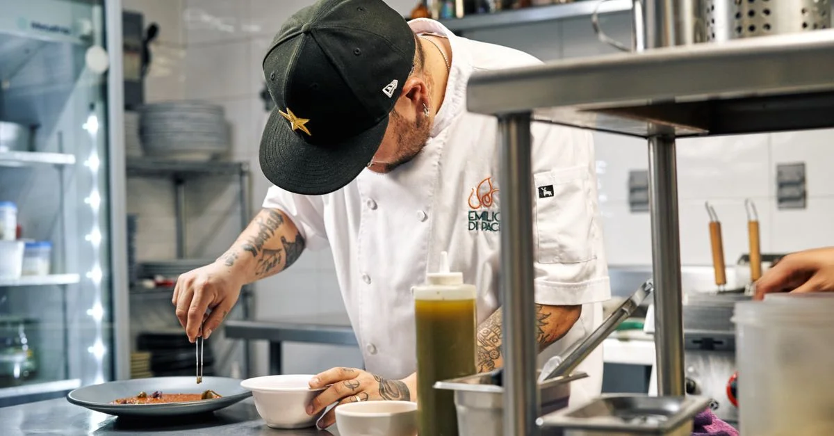Chef dans une cuisine professionnelle peignant soigneusement un plat avec précision et art.