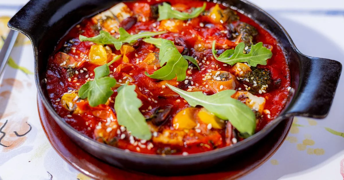 Ragoût de légumes fraîchement préparé garni de roquette, servi dans une poêle noire.
