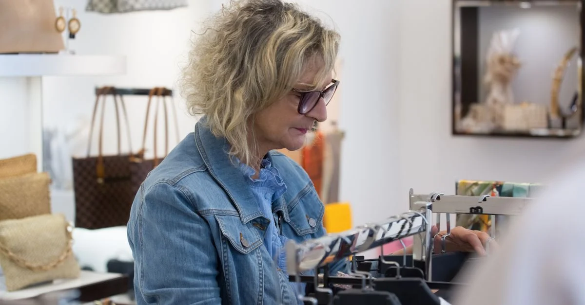 Femme âgée explorant des articles de mode dans une boutique, mettant en avant son style et son indépendance.