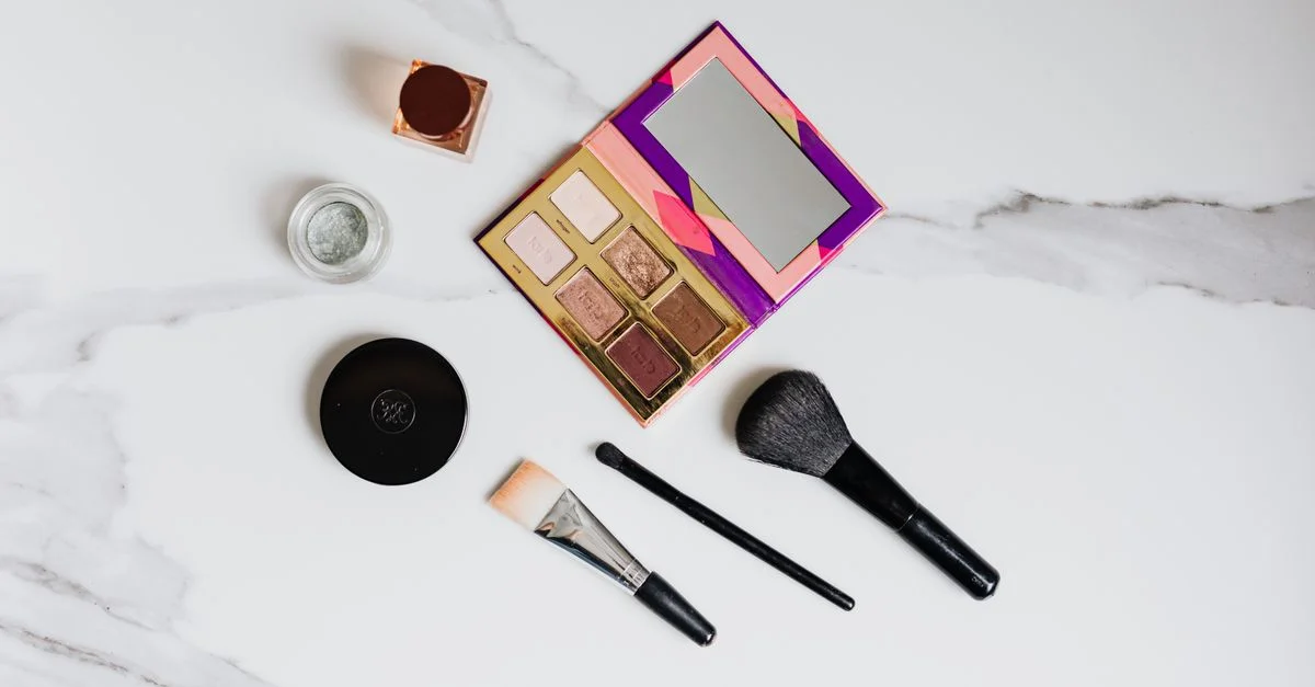 Disposition d'essentiels de maquillage sur un fond en marbre, mettant en avant des pinceaux et une palette de fards à paupières.