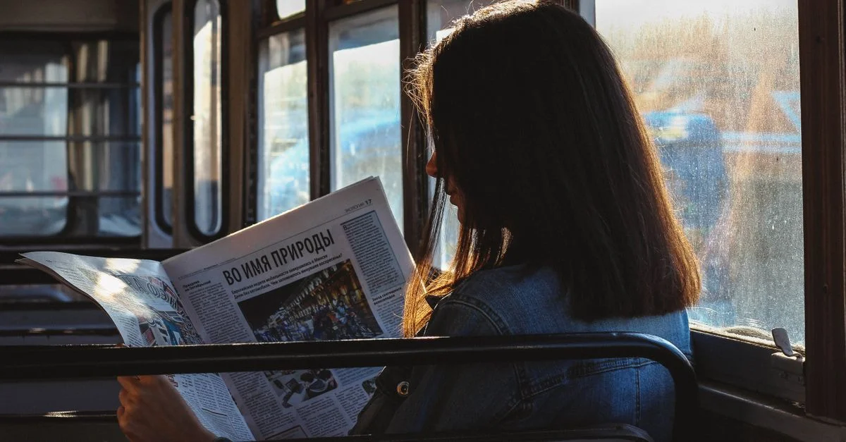 Une femme lit un journal dans un bus baigné de lumière, capturant un moment de réflexion silencieuse.