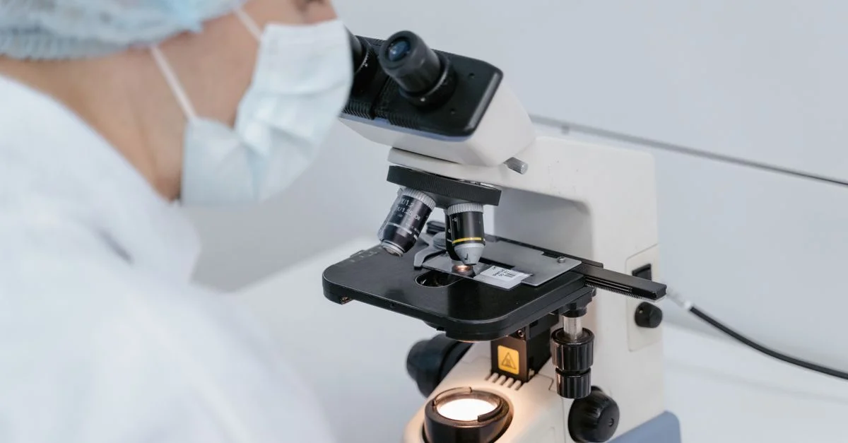 Scientifique utilisant un microscope dans un laboratoire, portant des équipements de protection.