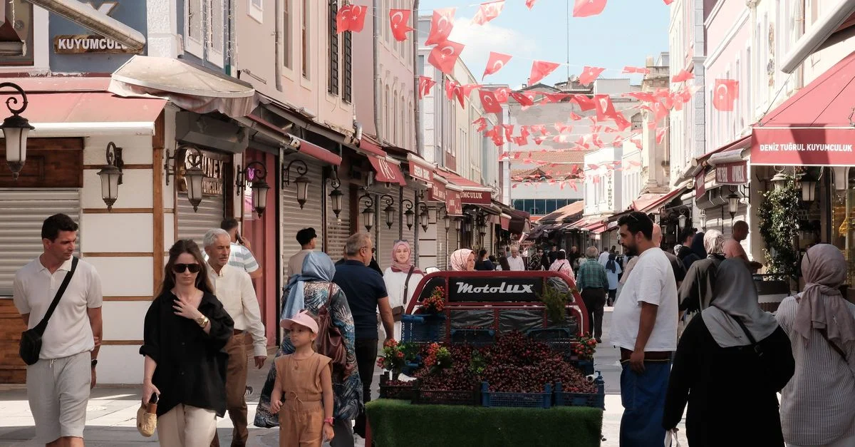 Scène de rue vibrante à Sakarya, Türkiye, avec des acheteurs et un vendeur de fruits sous des drapeaux turcs.