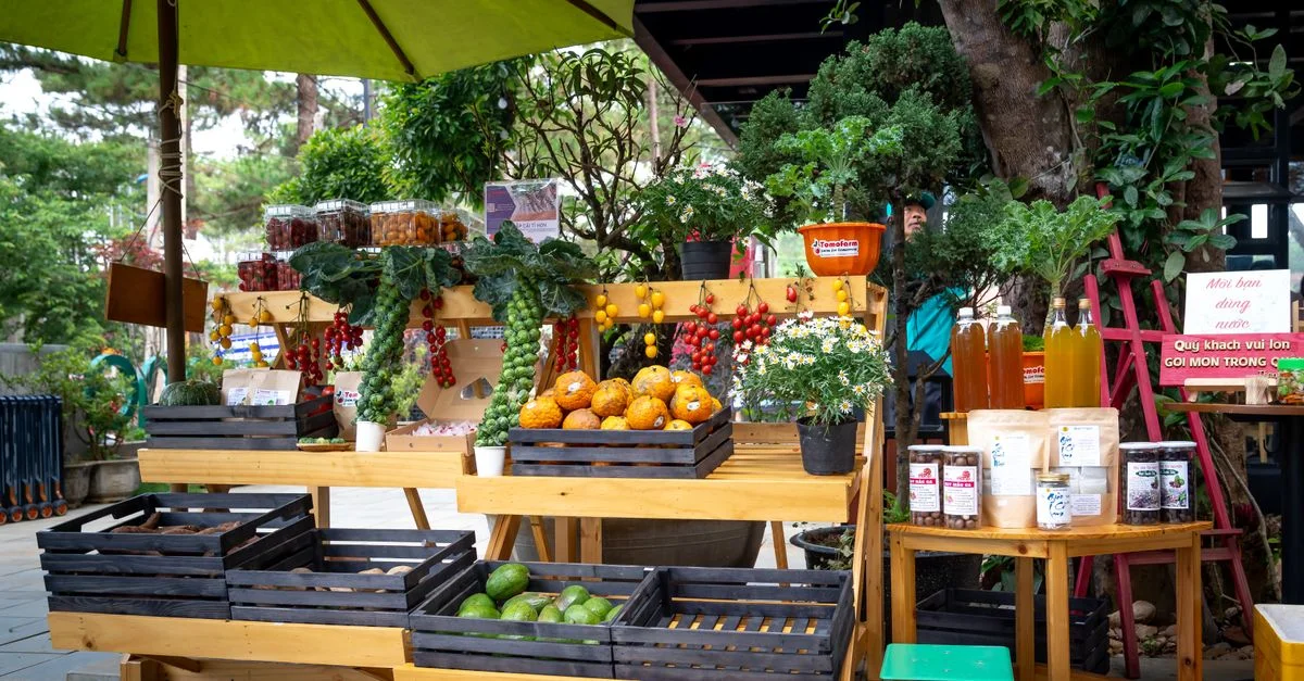 Un stand de marché en plein air coloré mettant en avant des fruits, des légumes et des produits frais sous un parapluie vert.