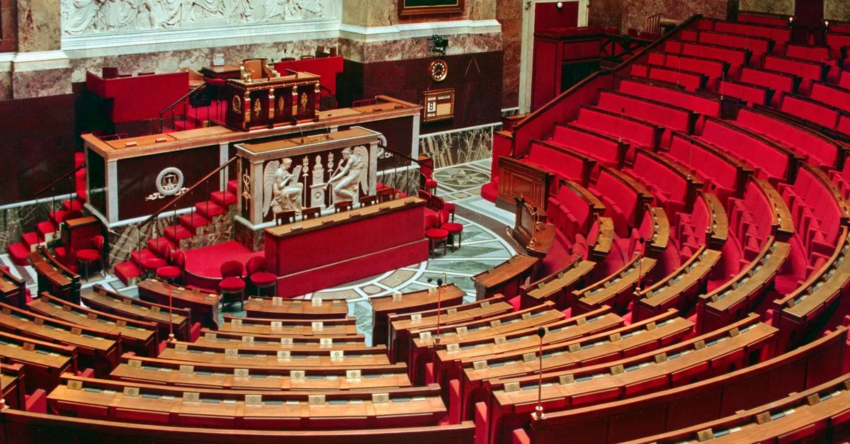 Vue lumineuse et élégante de l'intérieur riche de l'Assemblée nationale française avec des sièges rouges et un décor orné.