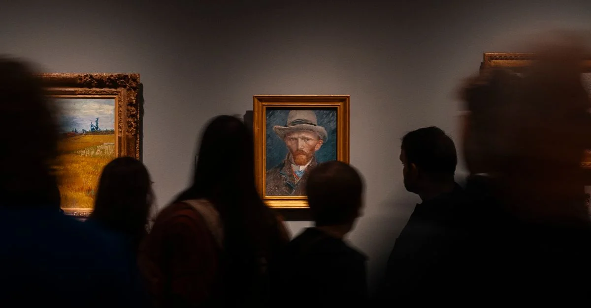 Des visiteurs, à l'ombre, observent un portrait de Van Gogh dans une galerie d'art, illustrant ainsi l'engagement culturel.