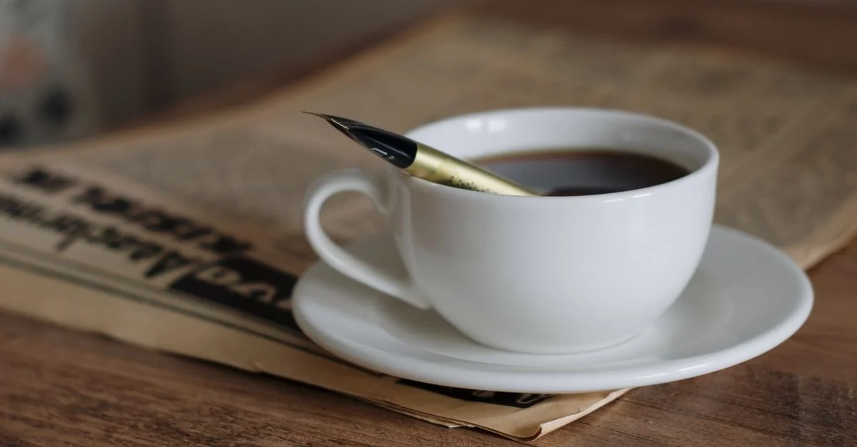 Un gros plan d'une tasse de café et d'un stylo plume sur une table en bois, évoquant une ambiance littéraire.