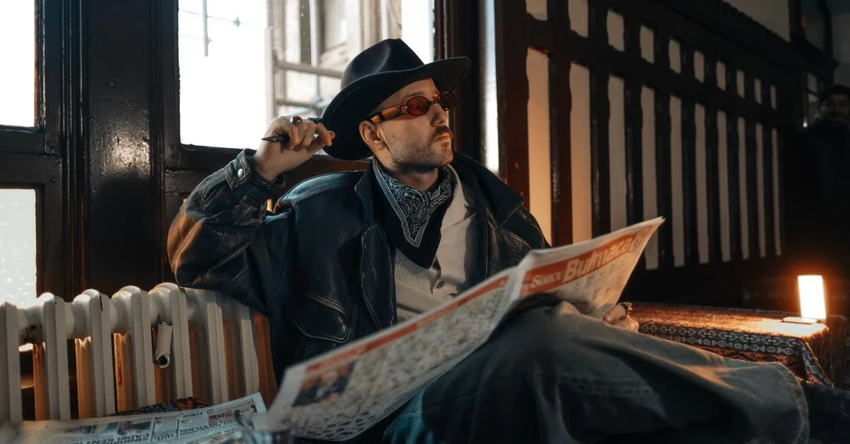 Homme élégant en cuir et chapeau lit un journal dans un décor vintage.