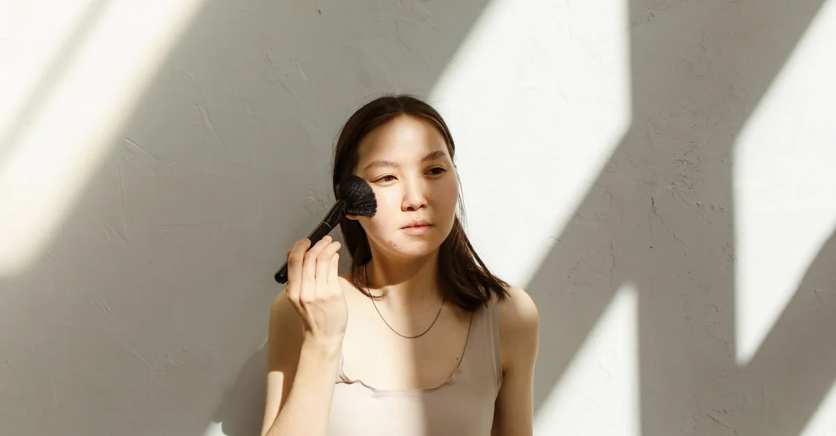 Femme asiatique appliquant du maquillage avec un pinceau à la lumière naturelle à l'intérieur.