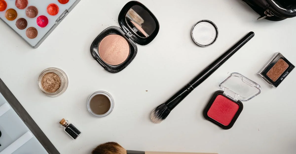 Un flat lay de produits de beauté comprenant des fards à paupières, des pinceaux et du blush sur une surface blanche.